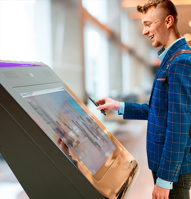 A man using a kiosk display at a reception desk in an office.